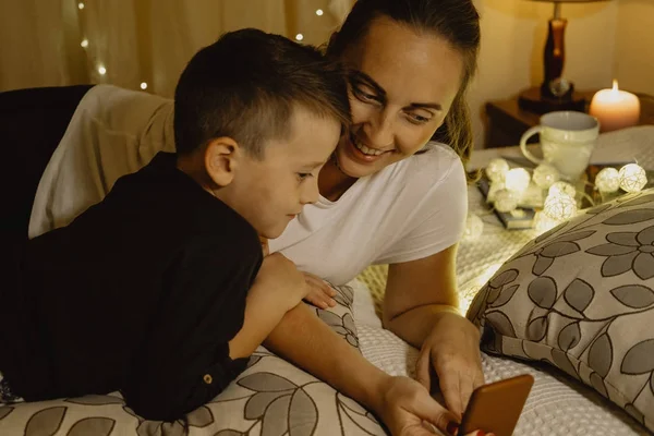 Mother and boy looking into the phone in bed before going to sle — Stock Photo, Image