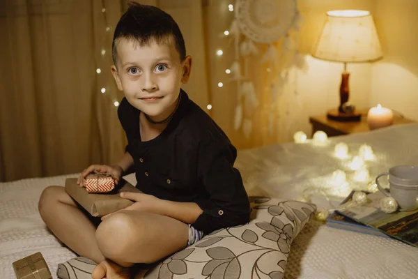 Ragazzo sorridente con regali nella camera di sera su un letto su un dorso — Foto Stock