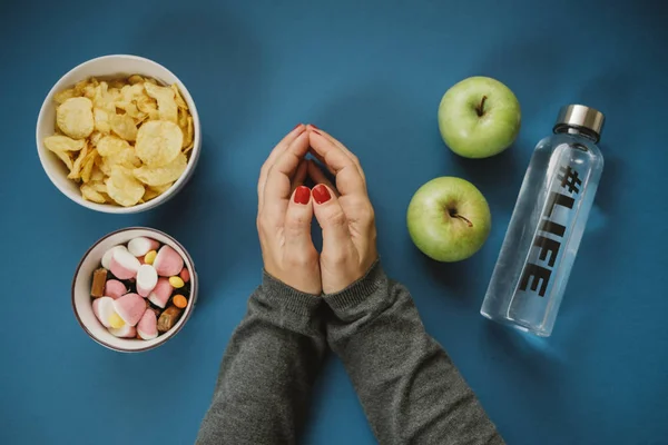 Ovanifrån med kvinna händer genom att välja apple eller vatten mot godis — Stockfoto