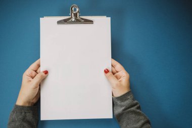 Mavi bir arka plan üzerinde beyaz bir sayfa tutan eller