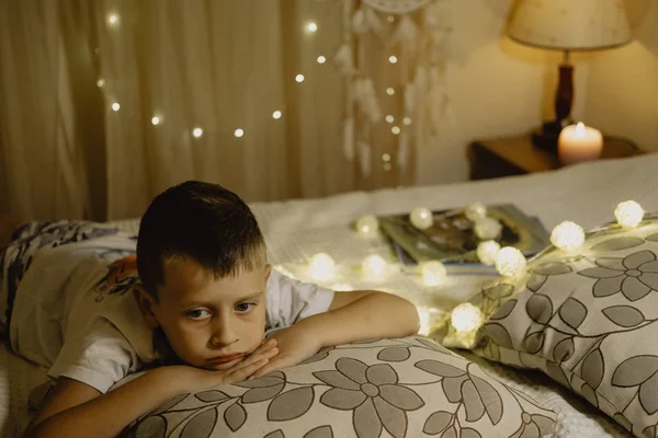 Портрет сумного хлопчика, що лежить у ліжку ввечері в темряві проти ба — стокове фото