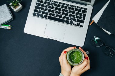 Kadın elleriyle yeşil smoothie ve siyah arka plan T üstünde laptop