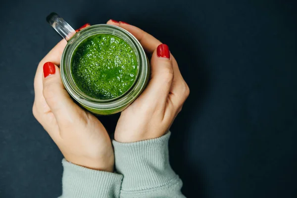 Manos de mujer con batidos verdes sobre una mesa negra — Foto de Stock