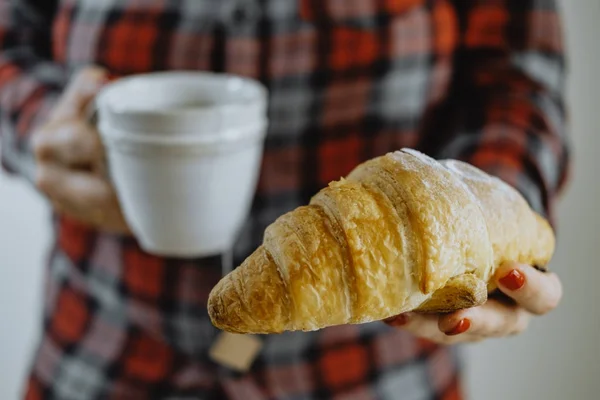 Vrouwelijke handen met kopje thee en een croissant — Stockfoto