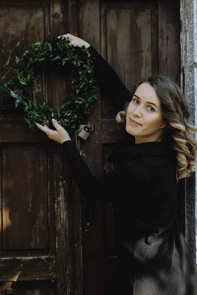 Retrato de mujer sonriente colgando una corona de Navidad en la puerta de — Foto de Stock