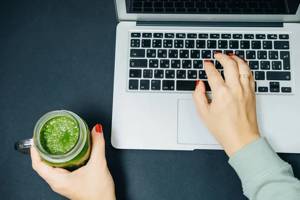  Kadın elleriyle yeşil smoothie ve siyah arka plan üstünde laptop.