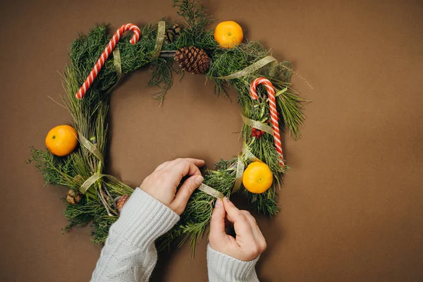 Woman hands with Christmas wreath on brown background. Top View — Stock Photo, Image