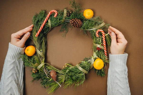 Woman hands with Christmas wreath on brown background. Top View — Stock Photo, Image