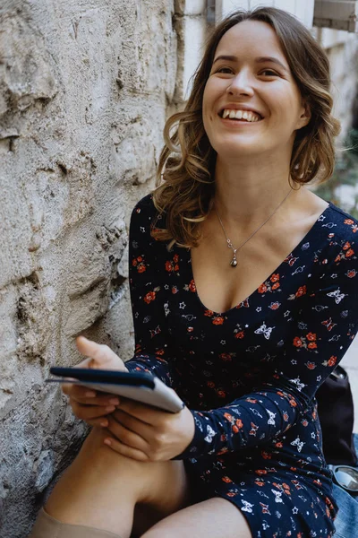 Joven mujer alegre leyendo un libro electrónico al aire libre — Foto de Stock