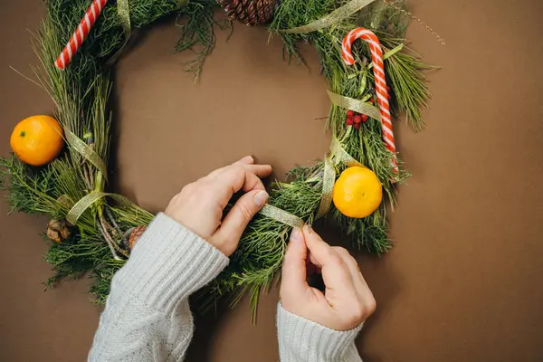Preparing for Christmas. Woman hands with wreath on brown backgr — Stock Photo, Image