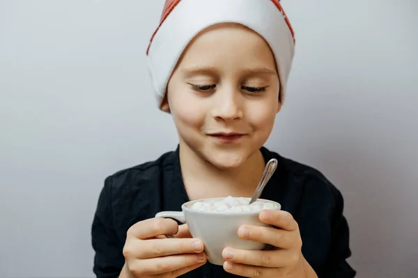 Roztomilý chlapec v červené čepici a pít kakao v hrnečku. Vánoční precizní — Stock fotografie