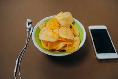 Kase cips, telefon ve kulaklık ile üstten görünüm üzerinde kahverengi backgr