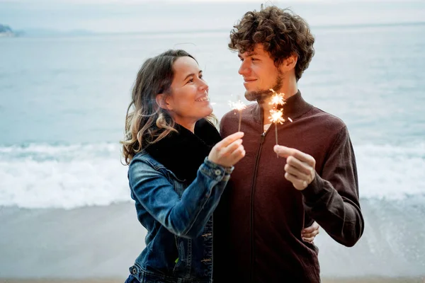 Sorrindo jovem casal feliz bonito segurando brilhos contra th — Fotografia de Stock