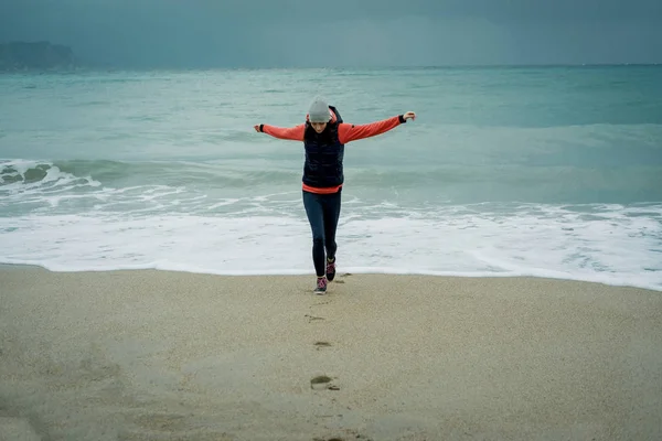 Vrolijke jonge vrouw staande op een koude winter strand en rek — Stockfoto
