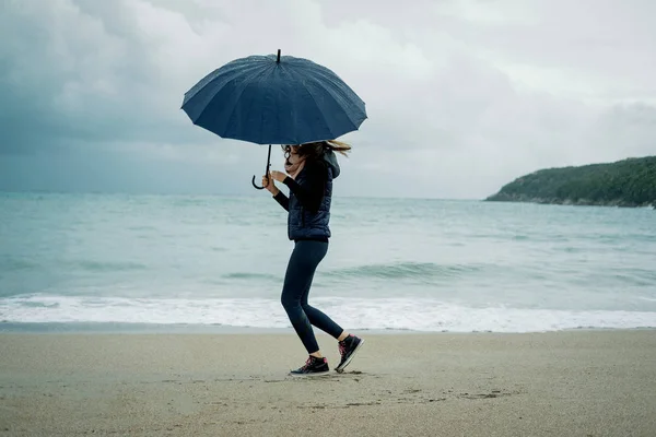 Smiling Young woman  runs from the wave with an umbrella in fron