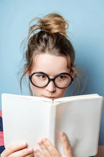 Pretty nerdy woman in spectacles reading a book against blue bac — Stock Photo, Image