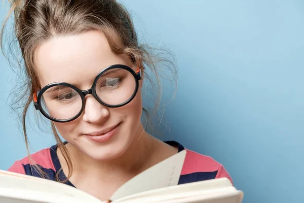 Genç kadın mavi bir arka plan üzerine bir kitap okur — Stok fotoğraf
