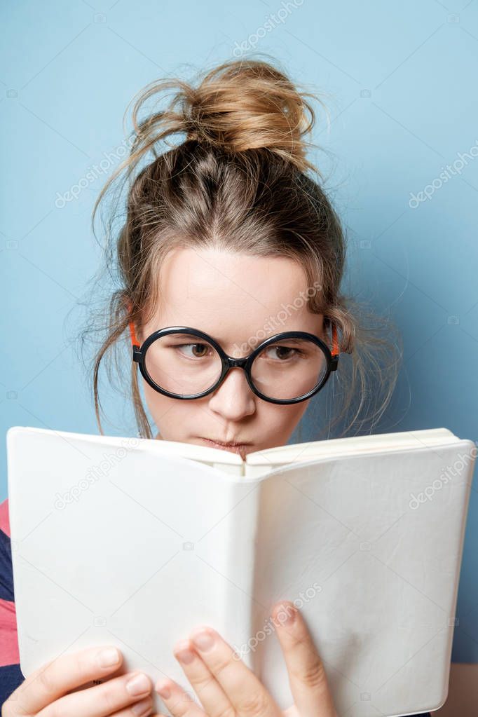 Pretty nerdy woman in spectacles reading a book against blue bac
