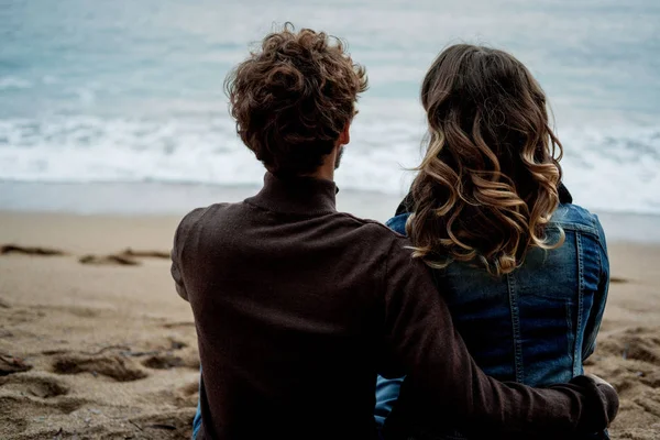 Rückansicht eines romantischen Paares, das am Strand sitzt und sich die — Stockfoto