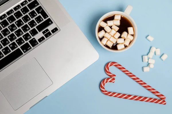 Cacau quente com marshmallows e laptop, doces em uma mesa azul . — Fotografia de Stock