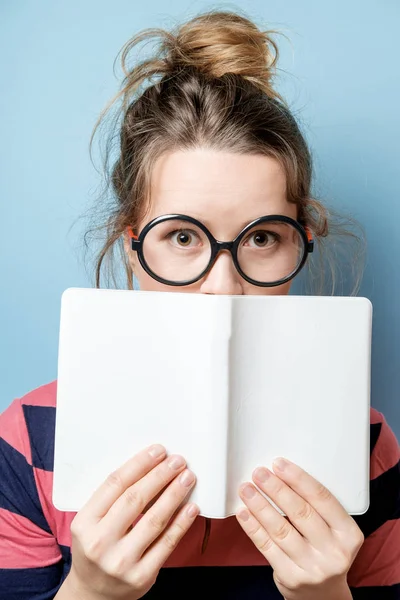 Mooie jonge vrouw leest een boek op een blauwe achtergrond — Stockfoto