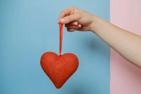 Mão de mulher com um coração em fundo rosa e azul. São Valentim — Fotografia de Stock