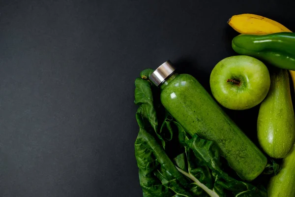 Verduras verdes y batidos en una botella de plástico en la espalda negra — Foto de Stock