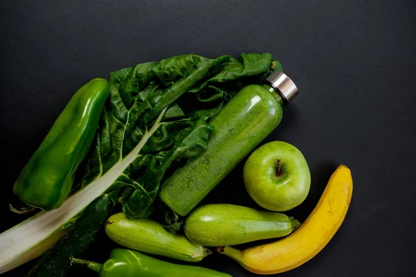 Verduras verdes y batidos en una botella de plástico en la espalda negra — Foto de Stock