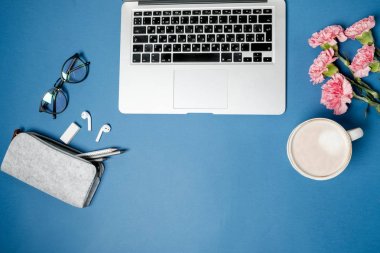 Düz yatıyordu kadın Ofis Masası. Laptop, pembe karanfil, kırtasiye mavi tablo ile çalışma alanı. Üstten Görünüm