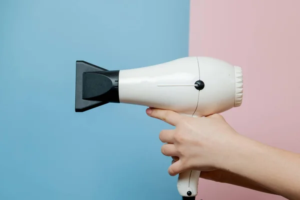 Woman hands with hair dryer on blue pink background. Beauty concept