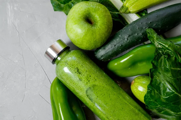 Green vegetables and smoothies in a plastic bottle on a gray background. Healthy concept. Top view, Space for text