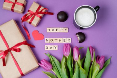 Mor laleler, hediye kutusu ve mor zemin üzerine ahşap harflerden oluşan buket. Anneler günü. Düz yatıyordu, en iyi görünümü