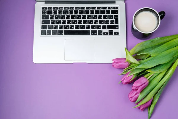 Woman desktop with Laptop, morning coffee and tulips on violet background. Flat lay, Spring holiday. Mother day