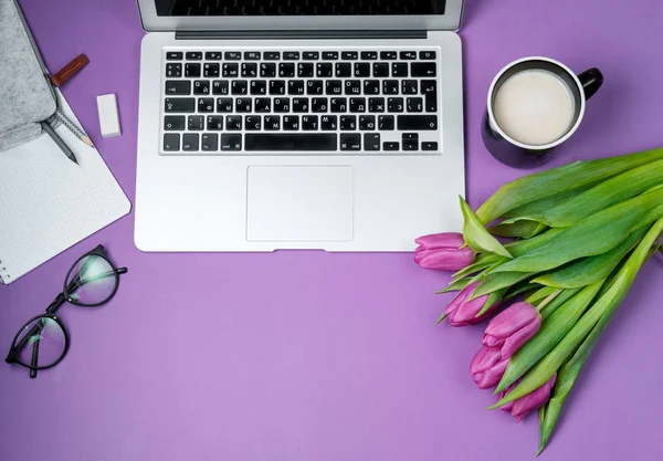 Laptop with morning coffee and tulips on violet background. Flat lay, Spring holiday. Mother day