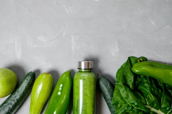 Green vegetables and smoothies in a plastic bottle on a gray background. Healthy concept. Top view, Space for text