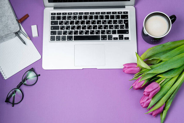 Женский рабочий стол с ноутбуком, утренний кофе и тюльпаны на фиолетовом b
