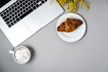 Kadın çalışma alanı laptop, Mimoza çiçeği, kruvasan, kahve ile bir