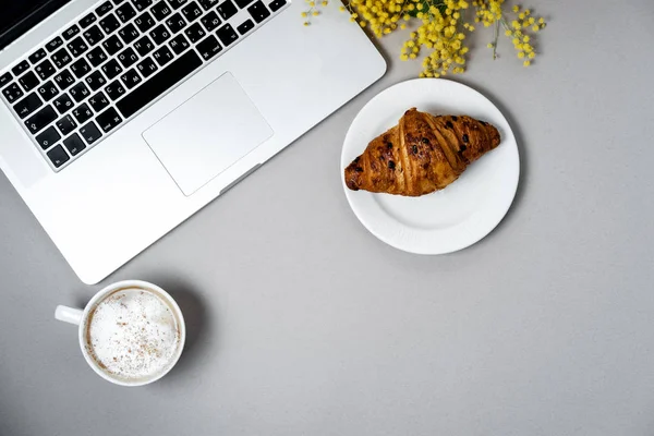 Vrouw werkplek met laptop, mimosa bloem, croissant, koffie een — Stockfoto