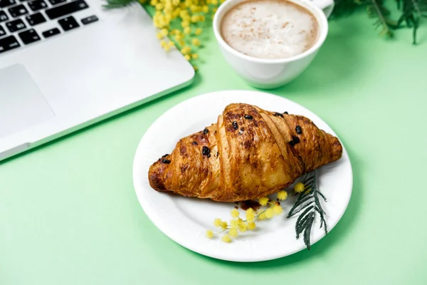 Woman work space with laptop, mimosa flower, croissant, coffee a