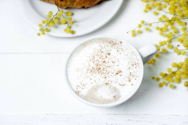 Croissant au chocolat et cappuccino, décoré de fleurs de mimosa — Photo