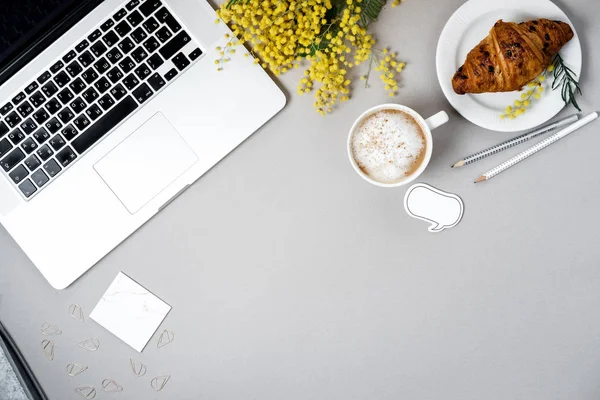 Vrouw werkplek met laptop, mimosa bloem, croissant, koffie een — Stockfoto