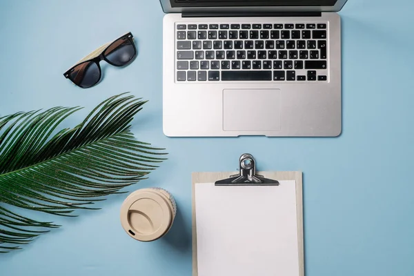 Робочий простір: ноутбук, пальмовий лист, кава і полуниця на блакитному — стокове фото