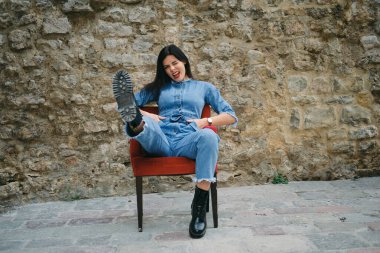 Kırmızı rujlu güzel, genç, gülümseyen esmer kadın arka planda bir koltukta oturuyor.