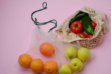 Pembe arka planda kumaş torbalarda meyve ve sebzelerin üst görüntüsü. Eko kavramı