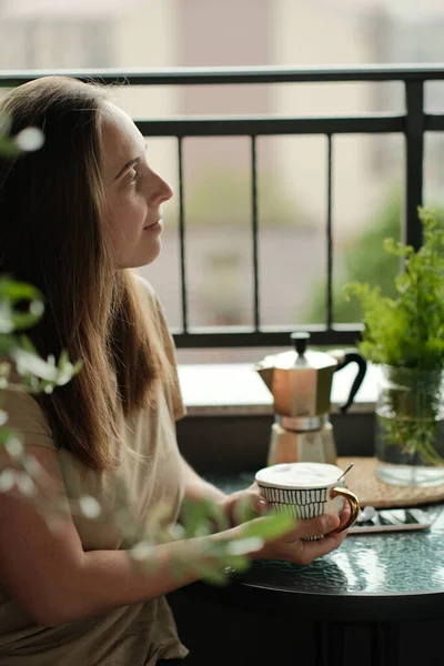 女性は植物と居心地の良いバルコニーでコーヒーを飲む — ストック写真