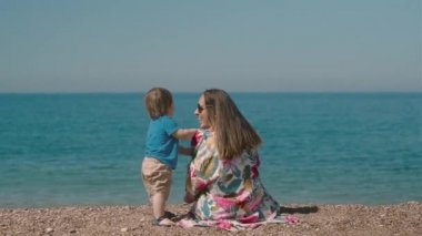 Gülen milenyum kadınının küçük bir çocukla oynaması ve güneşli bir günde deniz kenarında oturması. Anne ve oğul günlerini birlikte geçirirler.