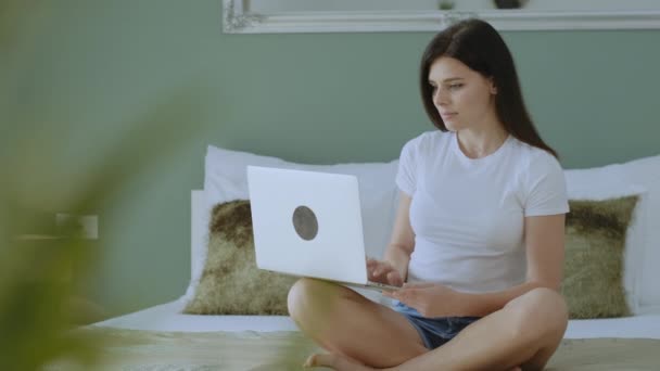 魅力的な女性のフリーランスは 自宅のオフィスから動作します ベッドの上に座ってノートパソコンをタイプしてコンピュータ画面を見て — ストック動画