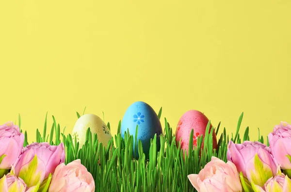 Huevos de Pascua pintados y flores rosadas en un cubo de hierba verde . — Foto de Stock