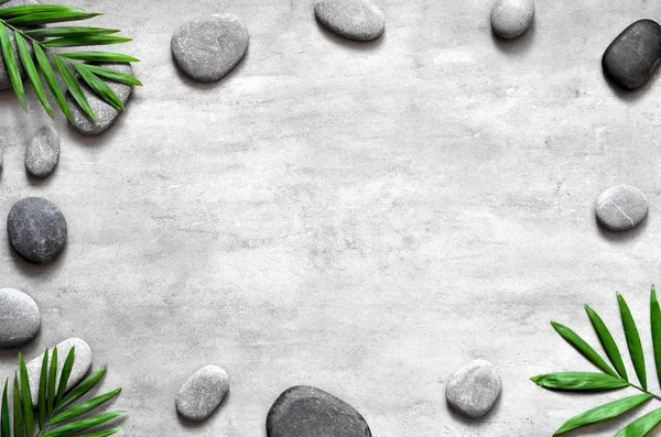 Grey spa background, palm leaves and grey stones, top view