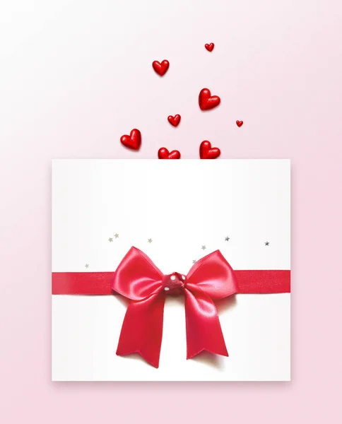 Червоні серця і білий конверт з бантом на рожевому фоні . — стокове фото